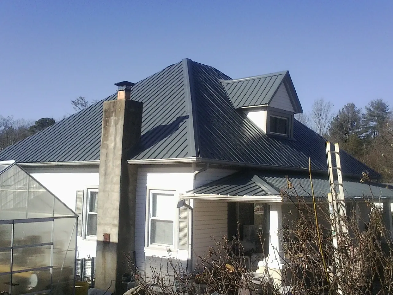 Dark blue standing seam metal roof on a white farmhouse with dormer — Slate & Tile Roof Repair by Roofing Brothers in Pierson