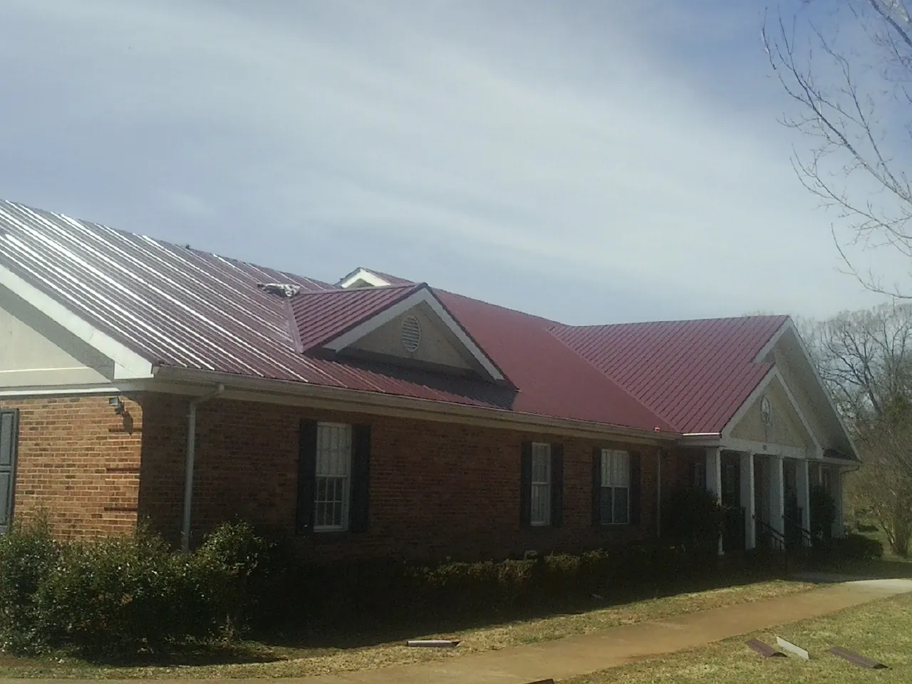Red metal roof with gabled entries on a long brick building, from a Hail Damage Roof Repair job in Pierson
